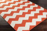 Close-up of the hand-woven Runnemede Area Rug. Coral and cream zigzags create a contemporary pattern on dark wood floors. Corner
