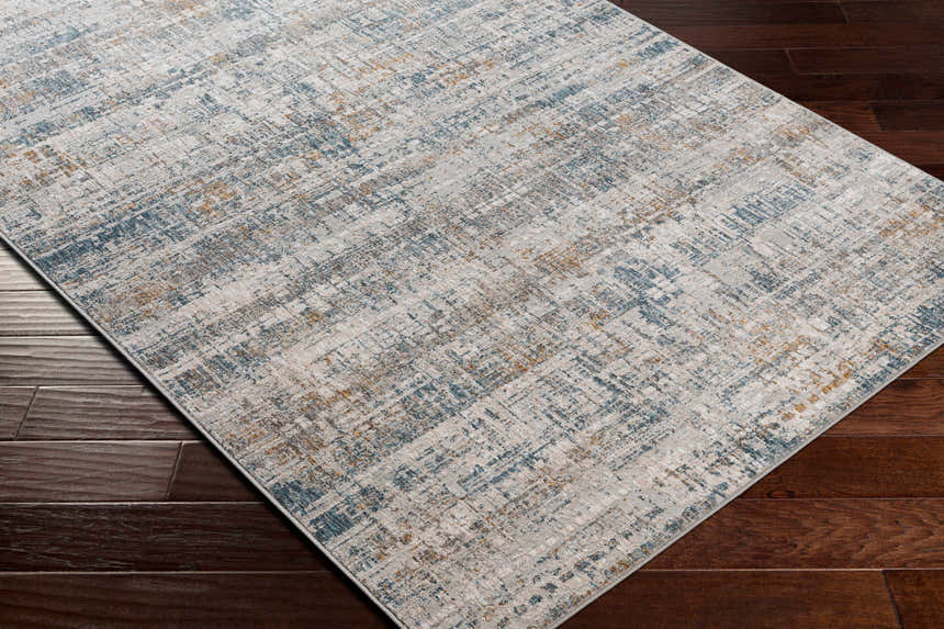 Close-up of the Runa Area Rug showing its contemporary blue, brown, and gray abstract design on a dark wood floor. Corner