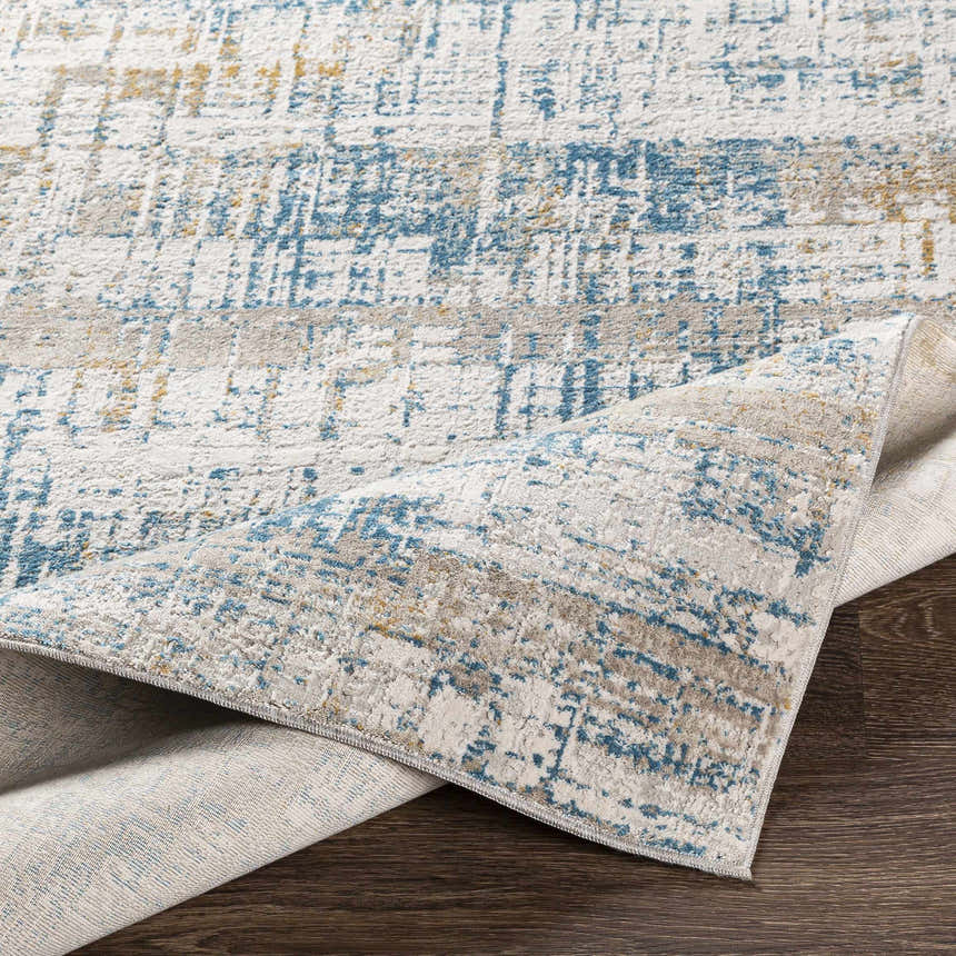 Close-up of the Runa Area Rug showing its blue, gray, mustard, and off-white contemporary pattern and soft polyester texture. Fold