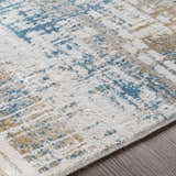 Close-up of the Runa Area Rug, a contemporary design in blue, mustard, and gray on an off-white base. Machine woven texture. Texture