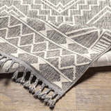 Close-up of the Reyn Area Rug featuring a gray and white geometric pattern and decorative tassels. Fold