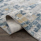 Close-up of the Liveri Abstract Blue Area Rug showing its blue, ivory, and mustard geometric pattern and machine-woven texture. Fold