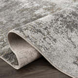 Close-up of the Liveree Abstract Area Rug showing light gray, medium gray, off white, and rust colors. Machine woven texture. Fold