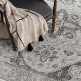 Close-up of the Liverpool Light Gray Area Rug with charcoal, gray, and mustard traditional pattern and a gray chair. Styleshot