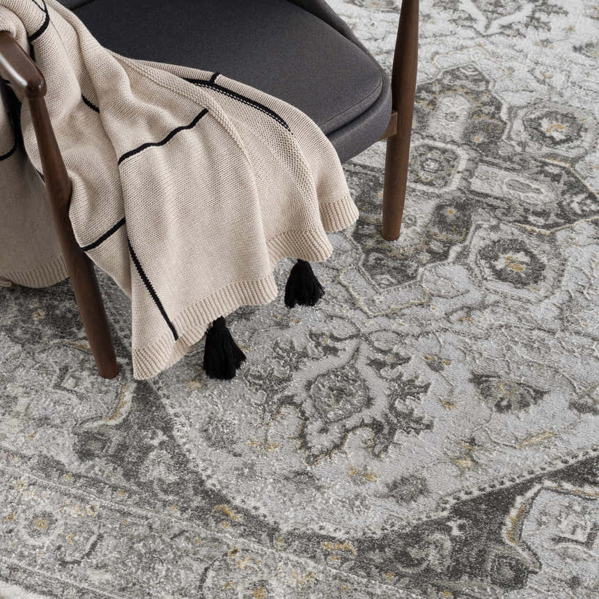 Close-up of the Liverpool Light Gray Area Rug with charcoal, gray, and mustard traditional pattern and a gray chair. Styleshot