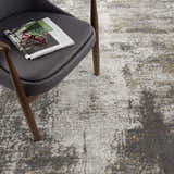 Close-up of the Liveree Abstract Area Rug in light gray, medium gray, off white, and rust colors, next to a gray chair. Styleshot