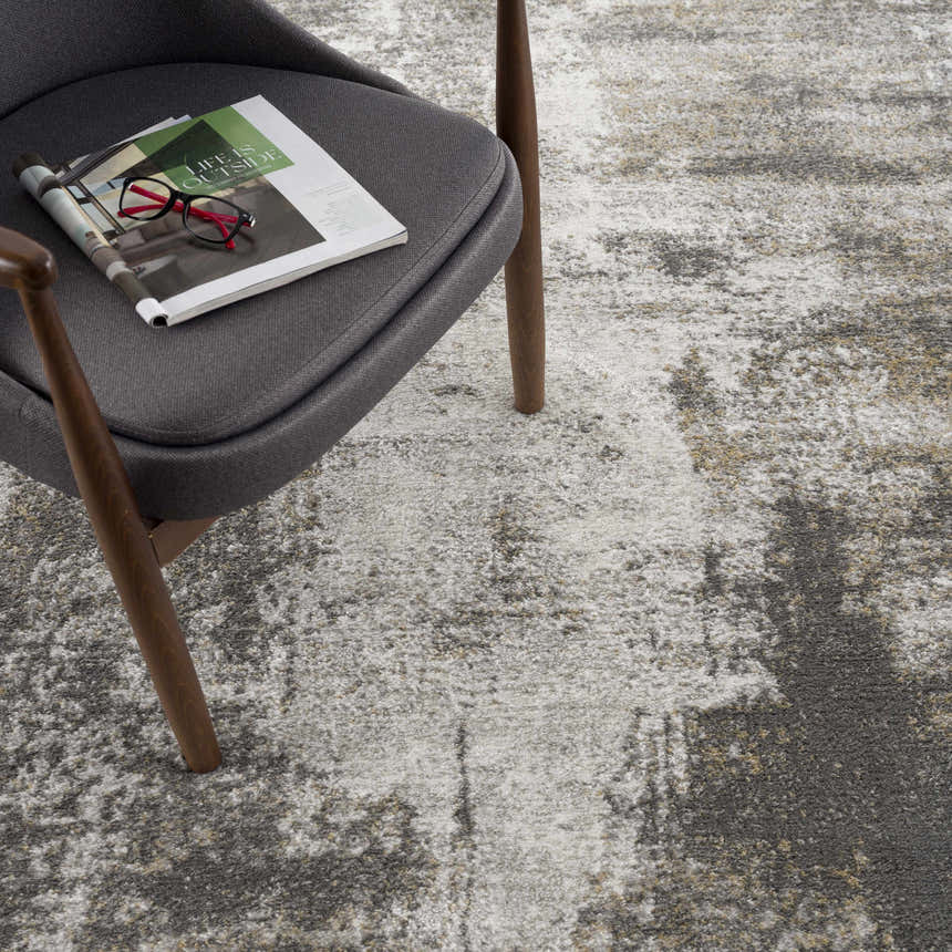 Close-up of the Liveree Abstract Area Rug in light gray, medium gray, off white, and rust colors, next to a gray chair. Styleshot