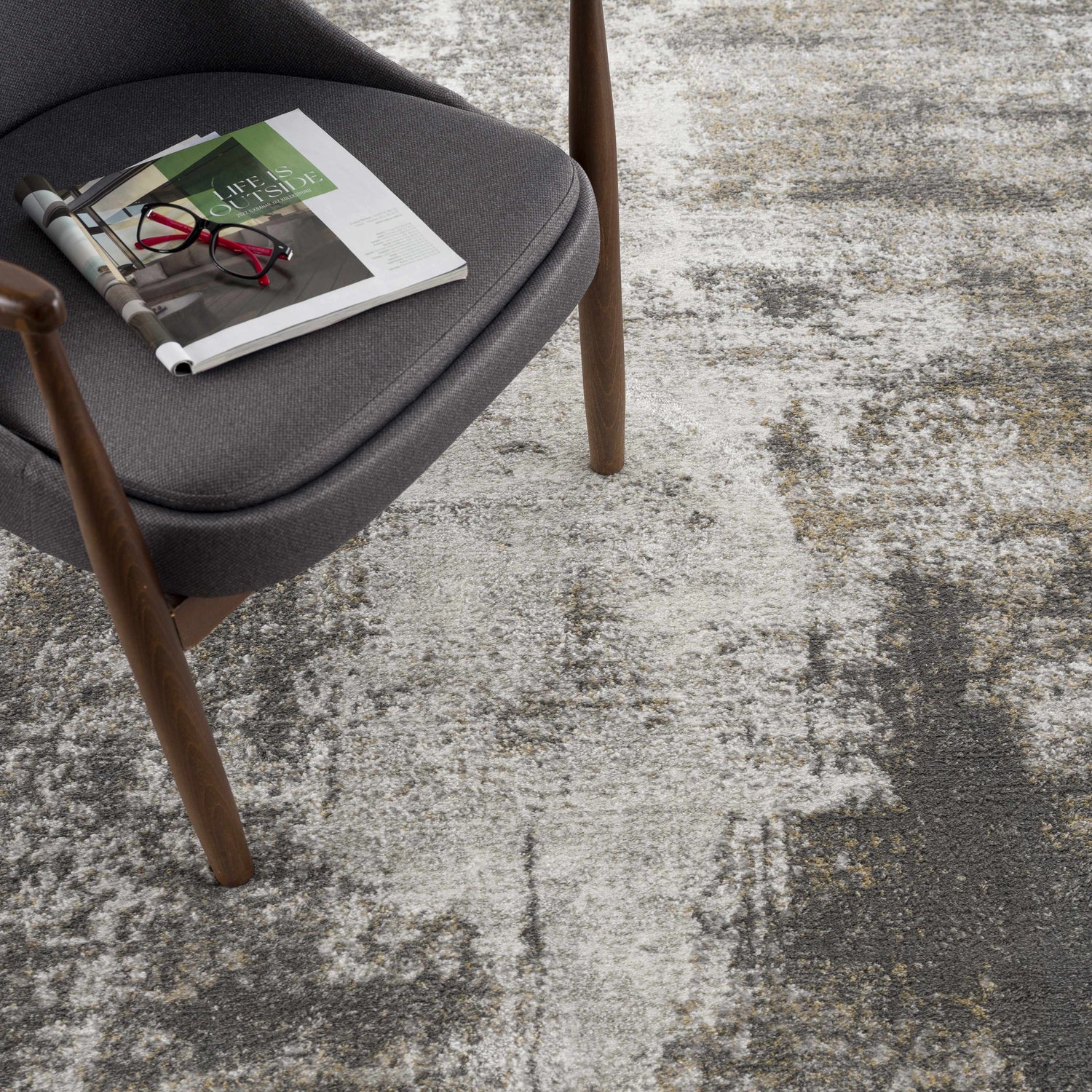 Close-up of the Liveree Abstract Area Rug in light gray, medium gray, off white, and rust colors, next to a gray chair. Styleshot