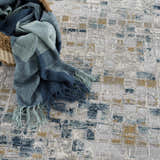 Close-up of the Liveri Abstract Blue Area Rug with a blue throw blanket in a basket. The rug has an abstract pattern. Styleshot