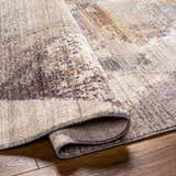 Close-up of the Birdy Area Rug showing its beige, brown, and gray contemporary design and soft, textured polyester material. Fold