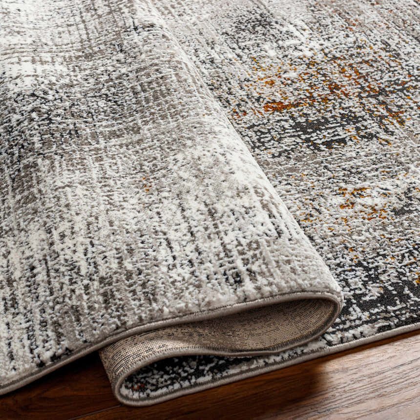 Close-up of the Ervin Gray Area Rug showing its charcoal, ivory, and rust abstract pattern and textured weave. Fold