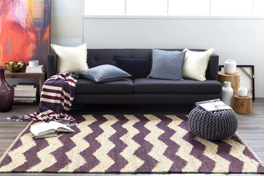 Living room scene with Saginaw Jute Carpet. Beige and dark purple chevron rug, gray sofa, and colorful art. Roomscene-Rectangle