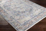 Close-up of the Salmo Area Rug showing its cream, denim, and brick red traditional pattern on dark wood floors. Corner