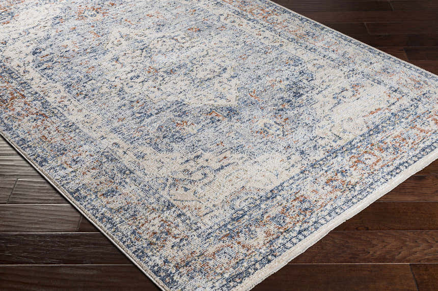 Close-up of the Salmo Area Rug showing its cream, denim, and brick red traditional pattern on dark wood floors. Corner