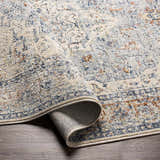 Close-up of the Salmo Area Rug showing its brick red, cream, and navy traditional pattern and soft, textured polyester material. Fold