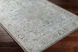 Close-up of the Anzu Washable Rug in light gray and taupe on a dark wood floor. Traditional farmhouse style rug. Corner