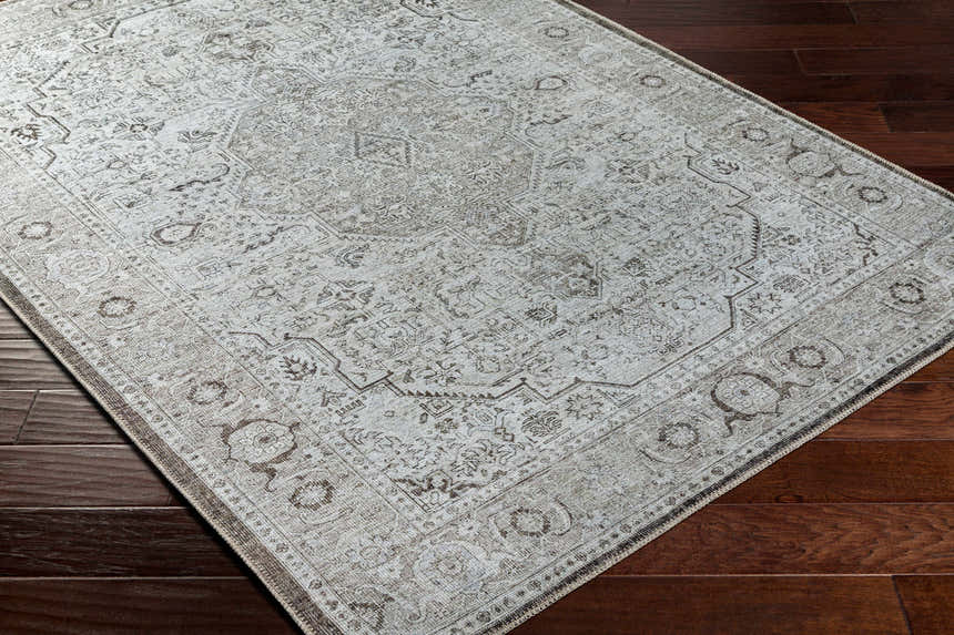 Close-up of the Anzu Washable Rug in light gray and taupe on a dark wood floor. Traditional farmhouse style rug. Corner