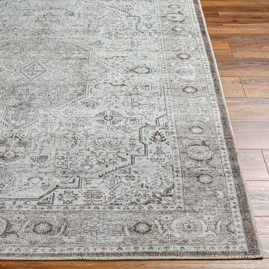 Close-up of the Anzu Washable Rug on wood floor. Traditional farmhouse style with charcoal, gray, and taupe floral pattern. Front