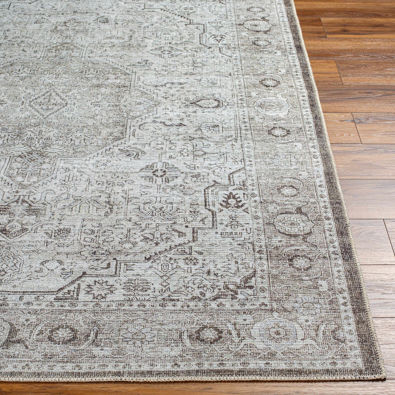 Close-up of the Anzu Washable Rug on wood floor. Traditional farmhouse style with charcoal, gray, and taupe floral pattern. Front