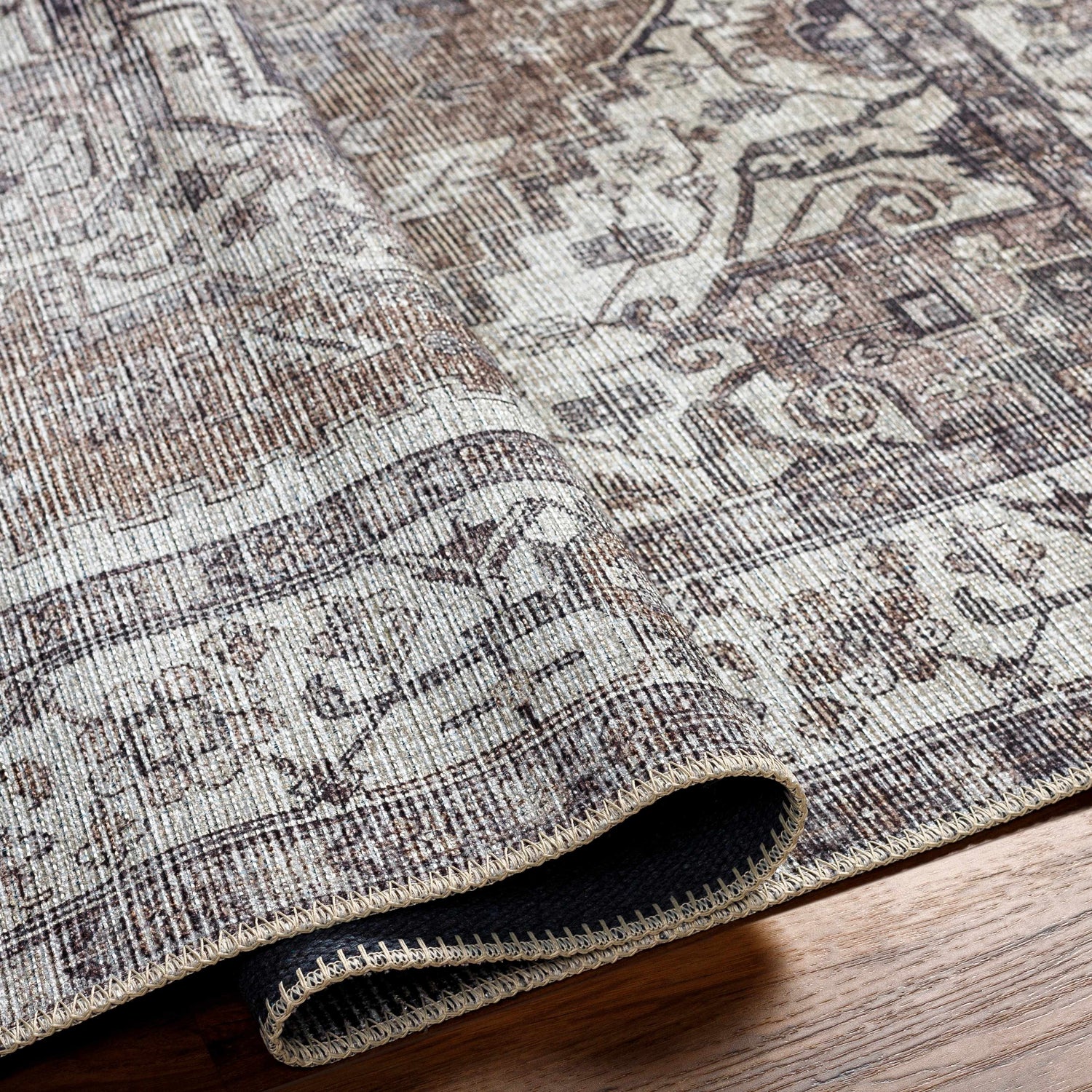 Close-up of the Athor Washable Rug showing its traditional, multi-brown pattern and woven texture on a wood floor. Fold