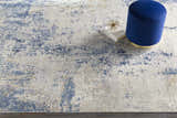 Close-up of the Sapcote Textured Luxe Area Rug in light beige and blue. Features a blue ottoman and decorative accents. Styleshot