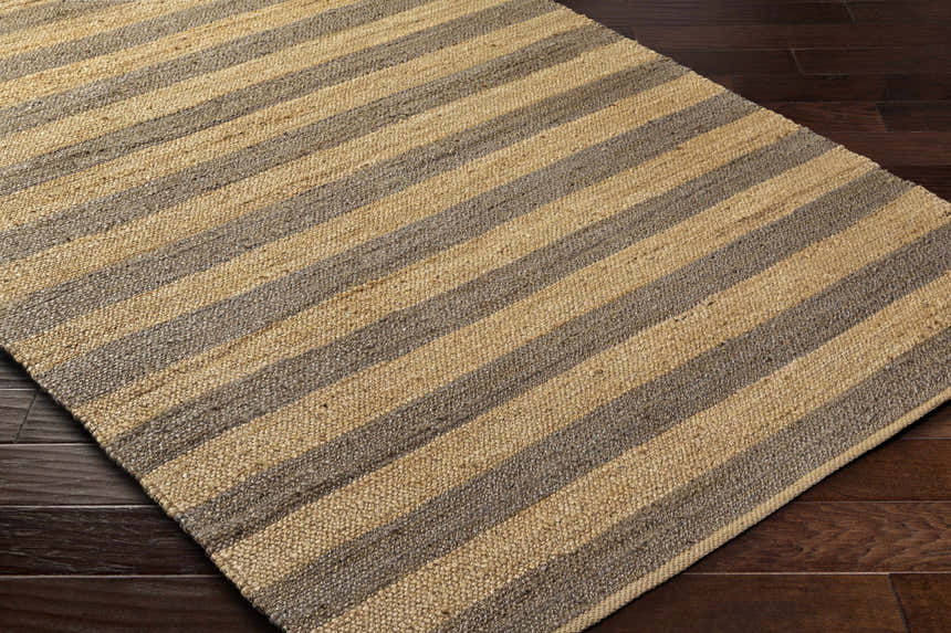 Close-up of the Ilkay Jute Area Rug. Camel and natural jute stripes. Hand-woven texture on dark wood floor. Farmhouse style. Corner