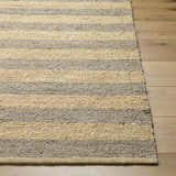 Close-up of the Ilkay Jute Area Rug showing its camel and natural jute stripes and hand-woven texture on a wood floor. Front