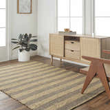 Living room scene with a camel and natural jute striped Ilkay Jute Area Rug, wood cabinet, and chair. Roomscene-Rectangle