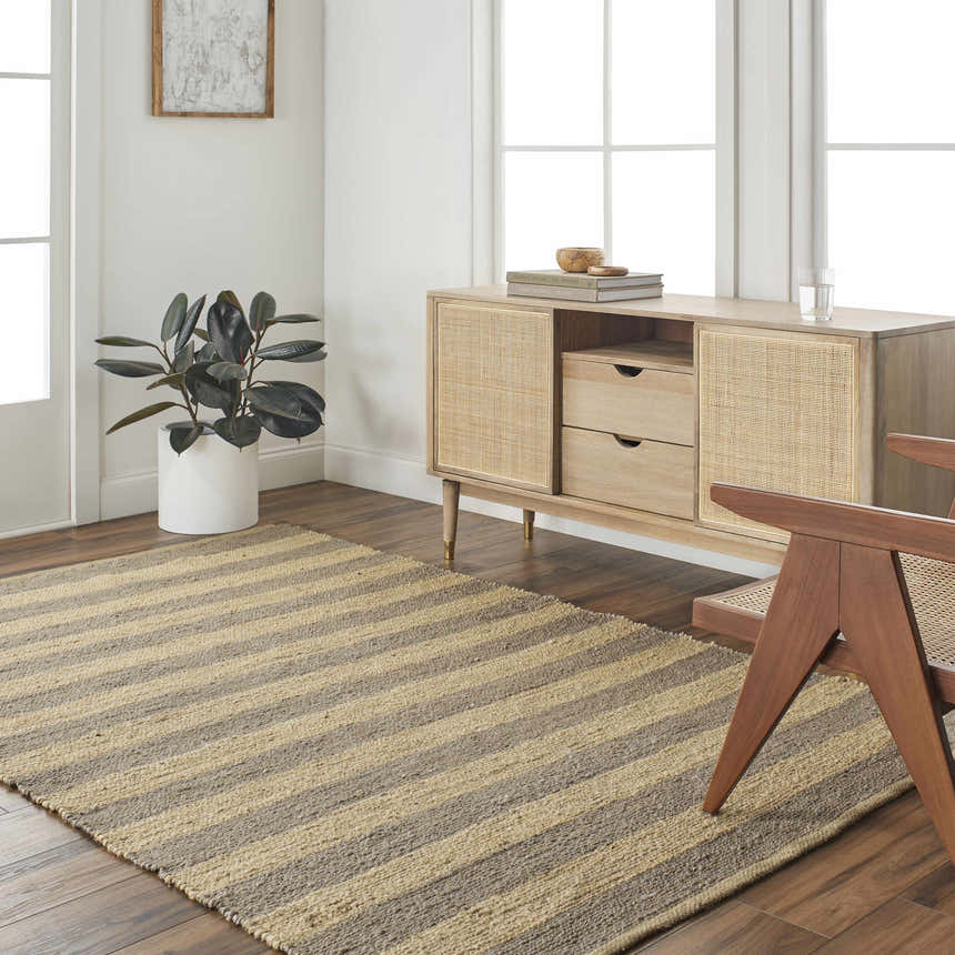 Living room scene with a camel and natural jute striped Ilkay Jute Area Rug, wood cabinet, and chair. Roomscene-Rectangle