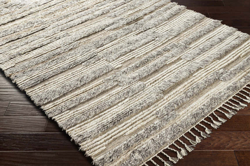 Close-up of the Saundersfoot Area Rug. Charcoal, gray, and beige wool rug with a striped, textured design and tassels. Corner