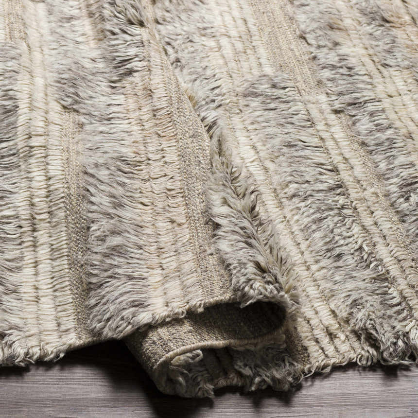 Close-up of the hand-knotted Saundersfoot Area Rug. Charcoal, gray, and light beige wool rug with a textured, bohemian design. Fold
