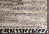 Close-up of the hand-knotted Saundersfoot Area Rug. Charcoal, gray, and light beige wool with a textured, bohemian design and fringe. Corner