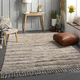 Living room scene with the textured Saundersfoot Area Rug in charcoal, gray, and beige. Bohemian style with a leather pouf and wood accents. Roomscene-Rectangle