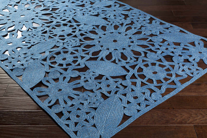 Close-up of the blue Sauquoit Area Rug showing its hand woven floral and leaf pattern on a dark wood floor. Corner