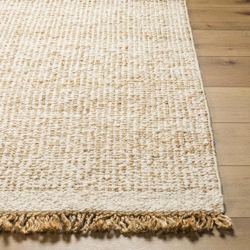 Close-up of the Gopi Jute Area Rug in Beige. Features a textured weave and fringed edge on a wood floor. Front