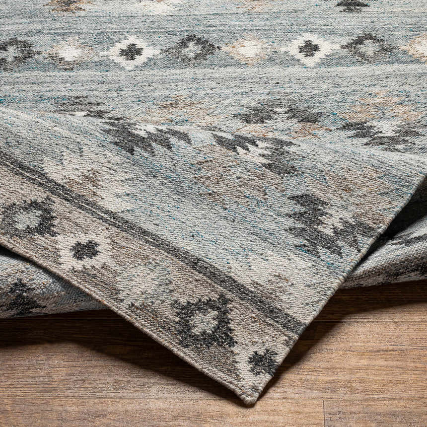 Close-up of the hand woven Denna Area Rug. Features a Southwestern inspired pattern in black, blue, brown, and white. Fold