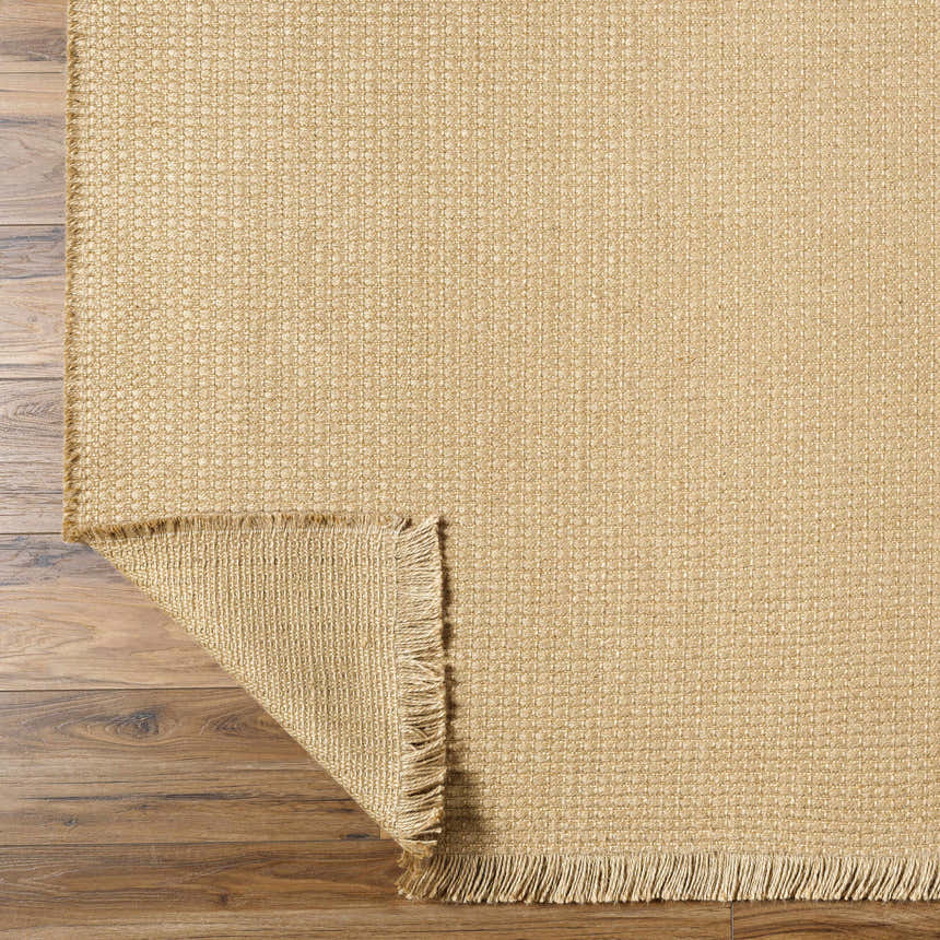 Close-up of textured Kimi Jute Light Beige Area Rug with fringed edge on a wood floor. Farmhouse style. Fold