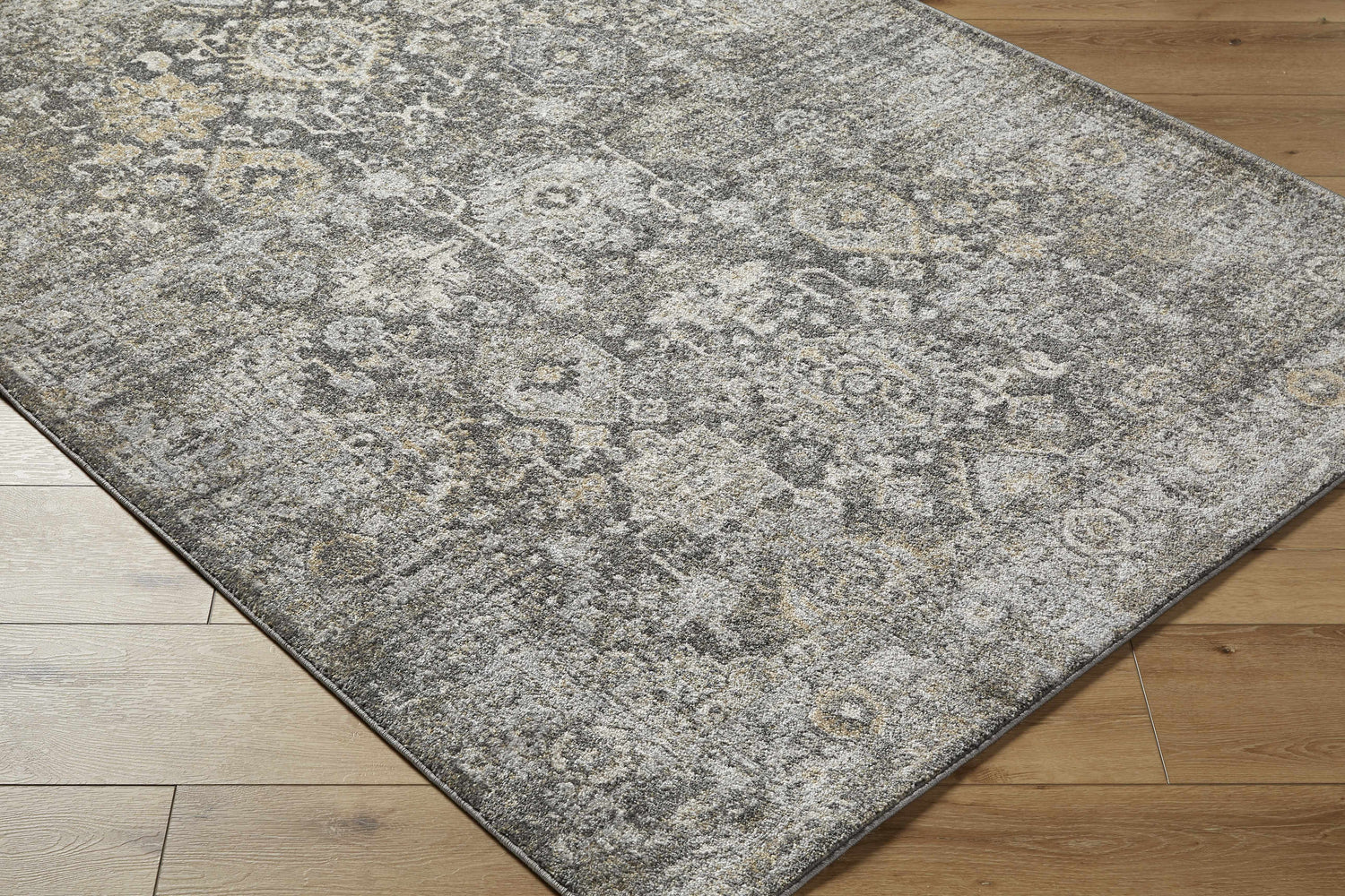 Close-up of the Strom Area Rug showcasing its traditional, distressed pattern in blue, charcoal, cream, and mustard tones. Corner