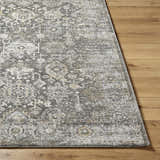 Close-up of the Strom Area Rug showing a traditional gray, cream, and mustard pattern on a wood floor. Front