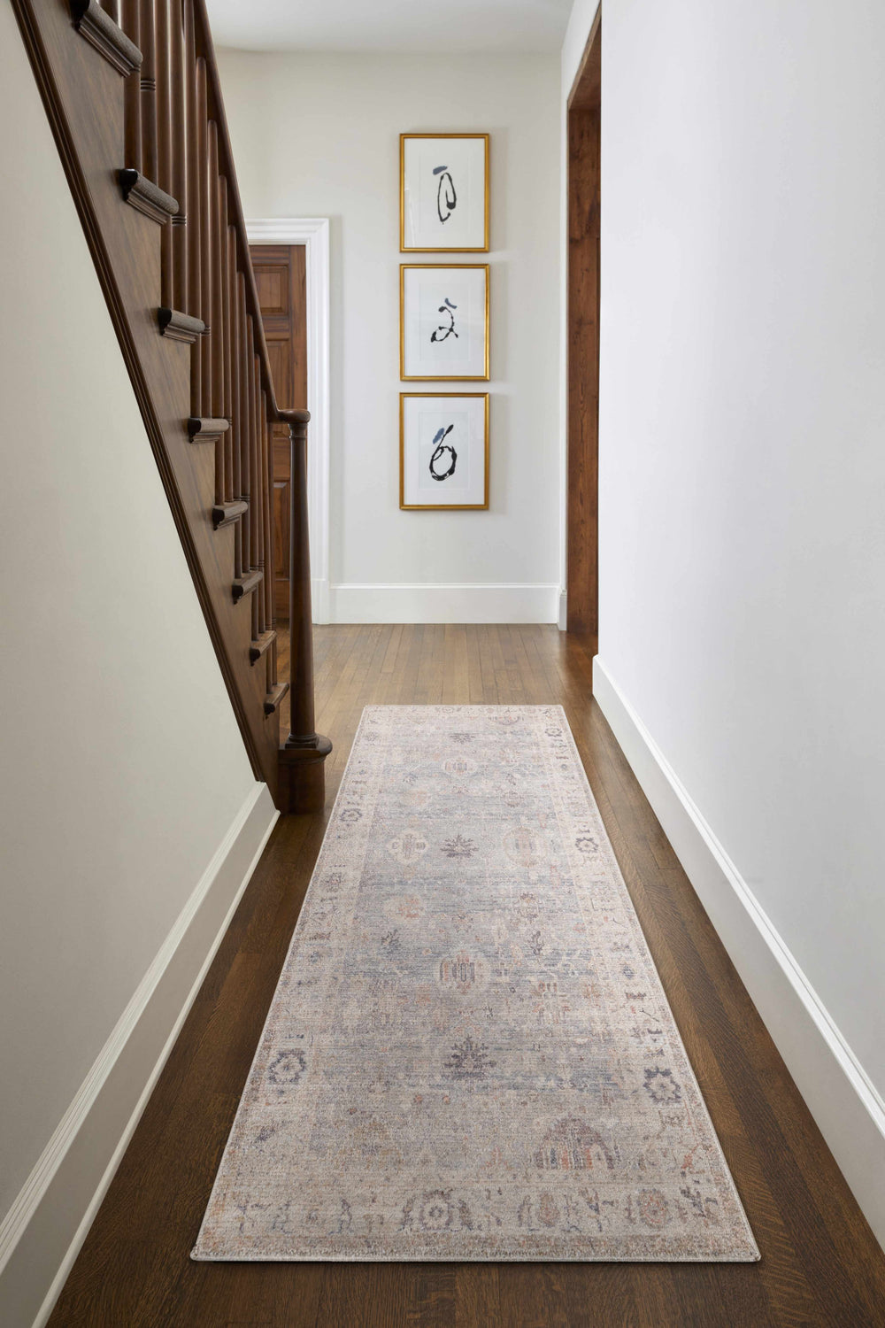 Hallway with wood floors and a Marlene Damask Cream & Blue Area Rug runner, staircase, and framed art. Roomscene-Runner