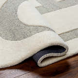 Close-up of the hand-tufted Adeja Area Rug. The wool rug features a geometric pattern in cloud gray and light gray tones. Fold