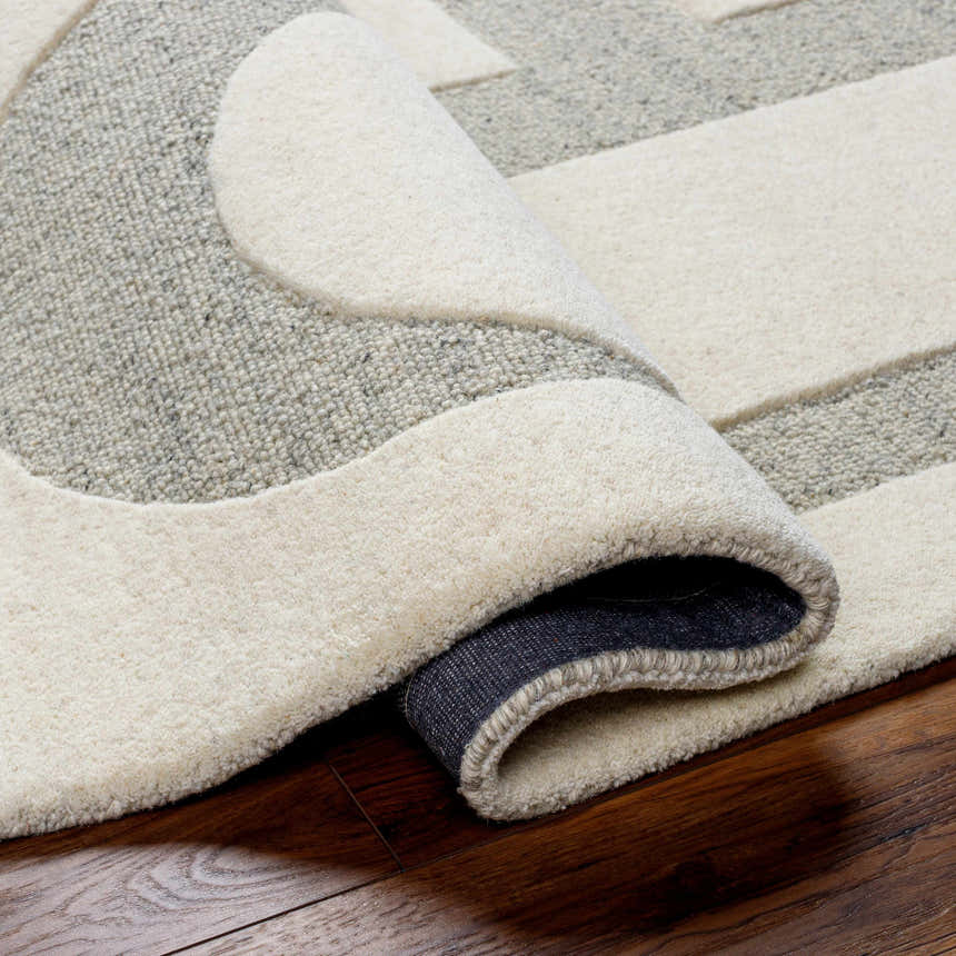 Close-up of the hand-tufted Adeja Area Rug. The wool rug features a geometric pattern in cloud gray and light gray tones. Fold