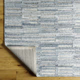 Close-up of the hand-tufted Darcy Area Rug. Features a textured, horizontal stripe pattern in blue, white, and tan hues. Fold