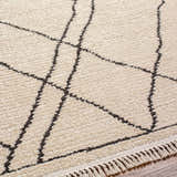 Close-up of the Ausca Area Rug, bone color with a dark brown geometric pattern and fringe detail. Texture