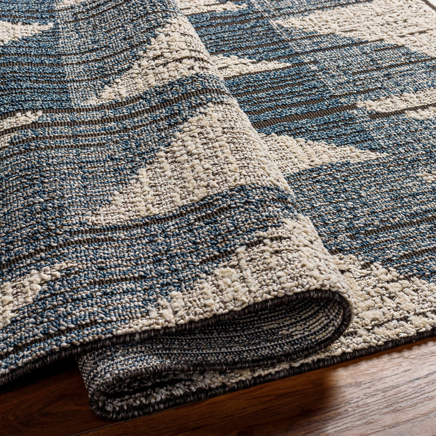 Close-up of Zaim Area Rug showing blue, beige, and brown geometric pattern and textured, machine-woven construction. Fold