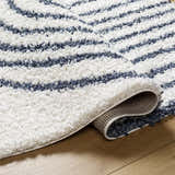 Close-up of the Jola Area Rug showing its geometric shag design in arctic stone and denim on a wood floor. Fold