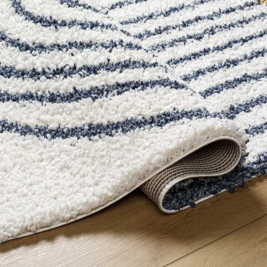 Close-up of the Jola Area Rug showing its geometric shag design in arctic stone and denim on a wood floor. Fold