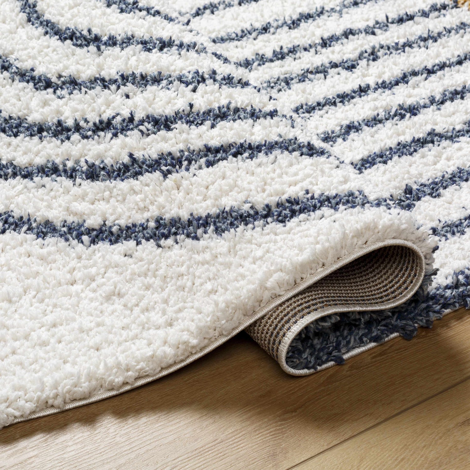 Close-up of the Jola Area Rug showing its geometric shag design in arctic stone and denim on a wood floor. Fold