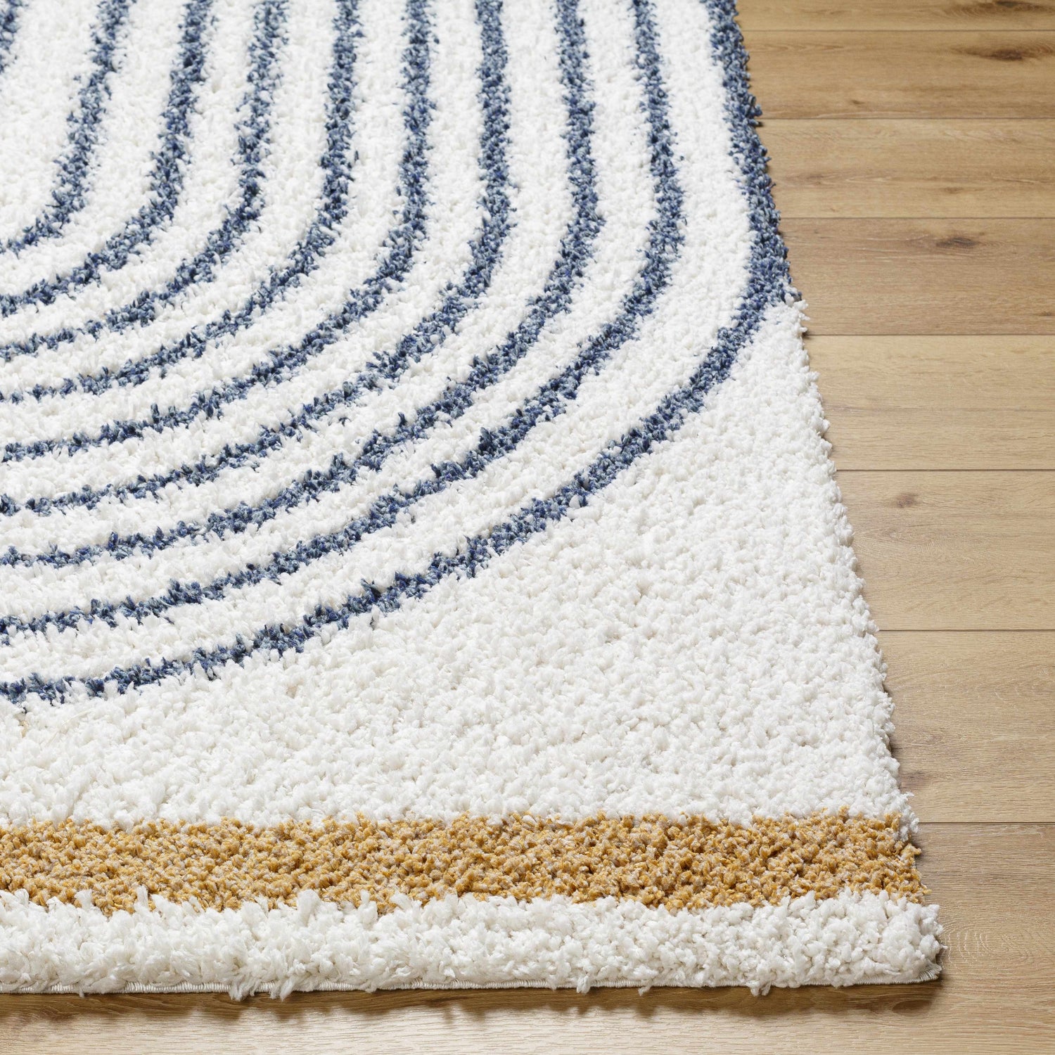 Close-up of the Jola Area Rug showing its white shag texture, blue geometric pattern, and tan accent stripe. Front