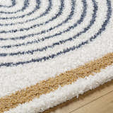 Close up of the Jola Area Rug showing its shag texture and geometric pattern in arctic stone, denim, and camel. Texture